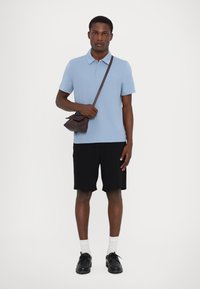 Lichtblauw poloshirt, zwarte shorts, zwarte schoenen, witte sokken, met een donkerbruine tas. Eenvoudig ontwerp, korte mouwen, klassieke pasvorm.