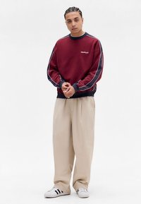 Vínová mikina s námořnickými akcenty, s kulatým výstřihem a logem na hrudi. Kombinována s béžovými volnými kalhotami a bílými teniskami.