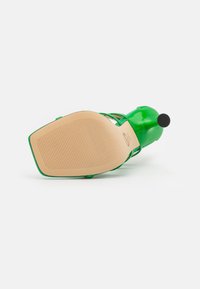 Sandalo verde con tacco alto, finitura lucida, suola in gomma texturizzata, design con cinturino e punta arrotondata. Accentuato da un piccolo dettaglio a forma di pallina nera.