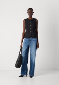 Svart ermeløs topp med rund halslinning og seks perleknapper, kombinert med lyseblå vide jeans og en svart kviltet håndveske.