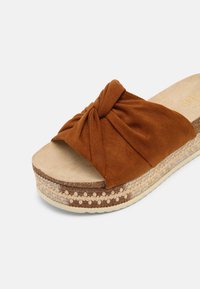 Sandale à glissière en daim marron avec sangle supérieure nouée et semelle plateforme tissée, semelle intérieure beige, présentée sous un angle sur fond blanc.