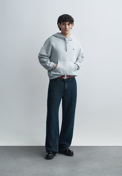 Γκρι φούτερ με κουκούλα, μπροστινή τσέπη και κορδόνι, συνδυασμένο με σκούρο τζιν παντελόνι. Το σύνολο συμπληρώνεται με κόκκινη ζώνη με μεταλλική αγκράφα.