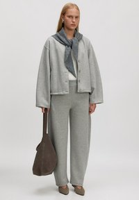 Grijze oversized sweatshirt met knopen, bijpassende grijze wijde sweatpants en een donkergrijze sjaal. Bruine schoudertas en grijze schoenen.