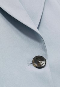 Vaaleansininen bleiserikangas, jossa on sileä pinta, ja siinä on erottuva tumma nappi, jossa on teksti "REISS", sekä viilto-kauluskaita.