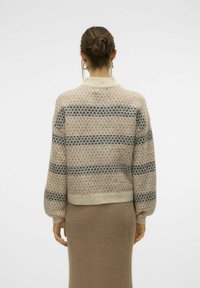 Pull court en maille beige avec des rayures géométriques bleu foncé et noires. Manches longues et ourlet côtelé, affichant une texture douce.