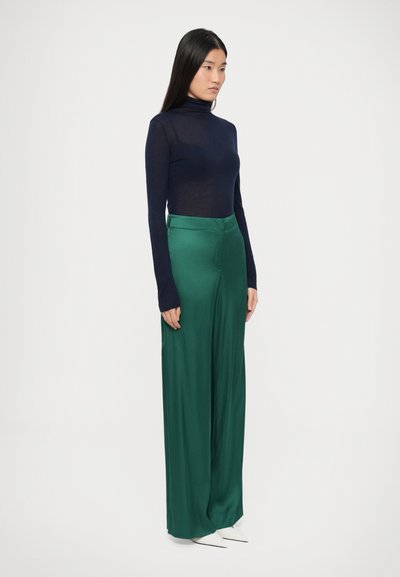 Merevärvi pika varrukaga kõrge kaelusega topp, kombineeritud kõrge vöökohaga laia lõikega roheliste pükstega. Sile kangas, voolujooneline istuvus ning peen läige.