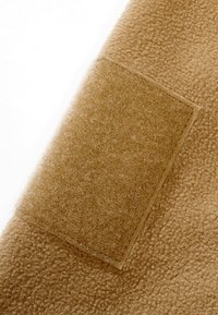Gros plan sur un tissu polaire beige avec un patch rectangulaire en velcro assorti cousu dessus.
