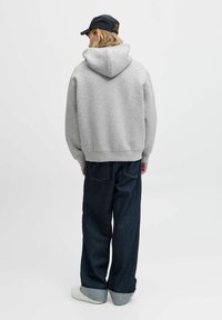 Grå hættetrøje med en stor hætte, parret med mørkeblå vide benjeans og hvide sneakers. Stoffet ser blødt og afslappet ud.