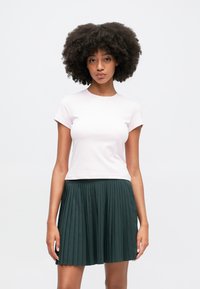 Jasnoróżowa koszulka z krótkim rękawem w połączeniu z ciemnozieloną plisowaną spódnicą, prezentującą gładką teksturę i dopasowany krój.