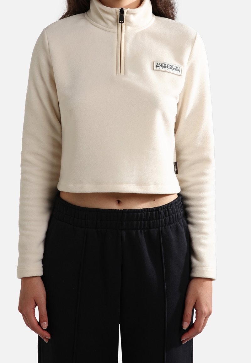 Sudadera corta de polar color crema con cremallera media, cuello alto y un pequeño parche de logo de la marca en el pecho. Tejido texturizado y suave.