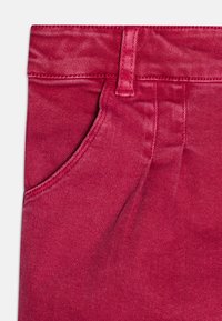 Pantalones de mezclilla rojo brillante con un bolsillo frontal, trabilla para el cinturón y costuras visibles. La tela tiene una textura suave con un aspecto ligeramente desvanecido.