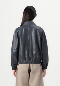 Giacca bomber in pelle blu navy con finitura testurizzata, polsini e vita elasticizzati, e colletto classico, vista dal retro.