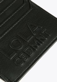 Musta nahkainen lompakko, jossa on kohokuvioitu "LOLA CUSDWANN" -teksti ulkopinnalla, ja se näyttää yksityiskohtaisen rakenteen ja ompelun.