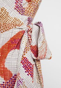 Tissu de robe multicolore avec des motifs dans des teintes orange, violet et marron ; présente un détail de nœud noué ; texture lisse et design léger.
