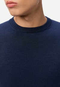 Marineblauer Strickpullover mit geripptem Rundhalsausschnitt und glatter Textur, Nahaufnahme des Stoffes und der Ausschnittdetails.