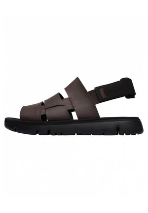 Brown synthetic sandals with a thick black sole, featuring interwoven straps and an adjustable black fabric heel strap for secure fit.