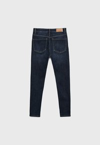 Jeans skinny de mezclilla oscura con una textura suave, que presentan dos bolsillos traseros y un parche de cuero en la cinturilla. Sin adornos visibles.