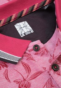 Rode en roze polo met een bloemenpatroon, gestructureerde stof en contrasterende zwart-witte gestreepte kraag. Bevat twee zwarte knopen.