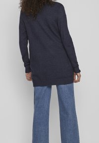 Langer marineblauer Cardigan mit einem strukturierten Strickdesign, gerippten Bündchen und Saum, kombiniert mit weit geschnittenen hellblauen Jeans.