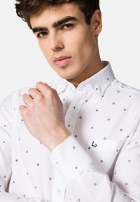 Biała koszula z guzikami z granatowym wzorem w gwiazdki, z kołnierzykiem i kieszenią z wyhaftowanym logo. Gładka tekstura i dopasowany krój.