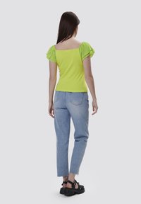 Grøn kortærmet top med flæser på ærmerne, parret med lyseblå straight-leg jeans og sorte platform sandaler.