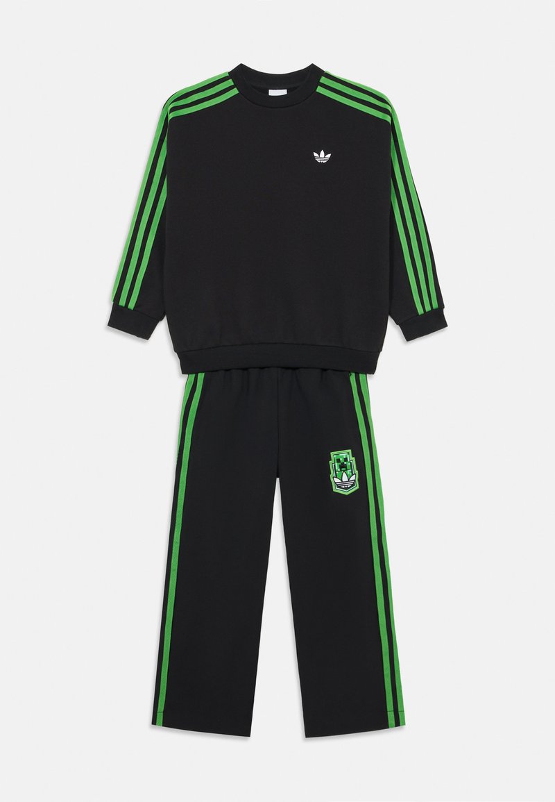 Schwarzes Sweat-Set mit grünen Streifen auf den Schultern und an den Seiten, begleitet von einem grafischen Logo auf der Hose. Weiches Material, lockere Passform.
