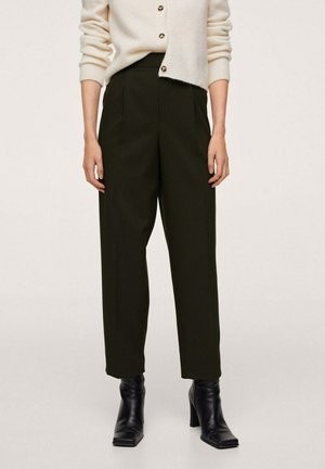 Mujer que lleva pantalones negros de talle alto y ajustados, y botines negros de tacón, combinados con un cárdigan crema abotonado.