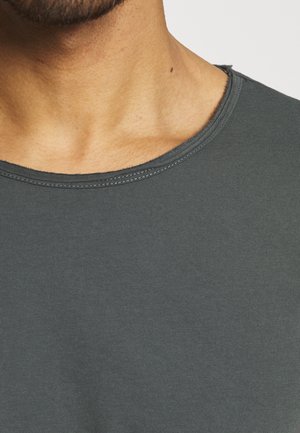 Nærbillede af en persons nakke og øverste bryst iført en mørkegrå t-shirt med rund hals og synlige sømme.