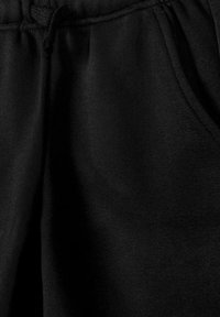 Pantalon de survêtement en tissu noir, avec taille élastique, cordon de serrage et détail de poche latérale en gros plan.