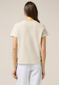 T-shirt couleur crème à manches courtes, texture en coton doux, encolure ronde et coupe décontractée, associé à un pantalon blanc.