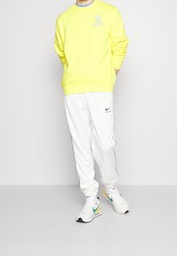 Jasně žlutá mikina s modrými detaily, kombinovaná s bílými tepláky s černými pruhy na bocích a logem Nike. Bílé tenisky s barevnými prvky.