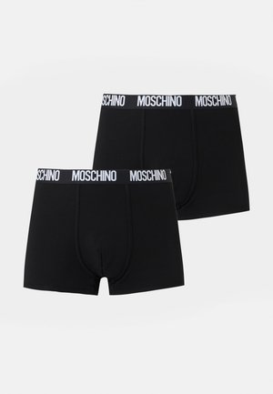 Dvě černé pánské boxerky s bílými gumami s nápisem "MOSCHINO" na jednobarevném pozadí.