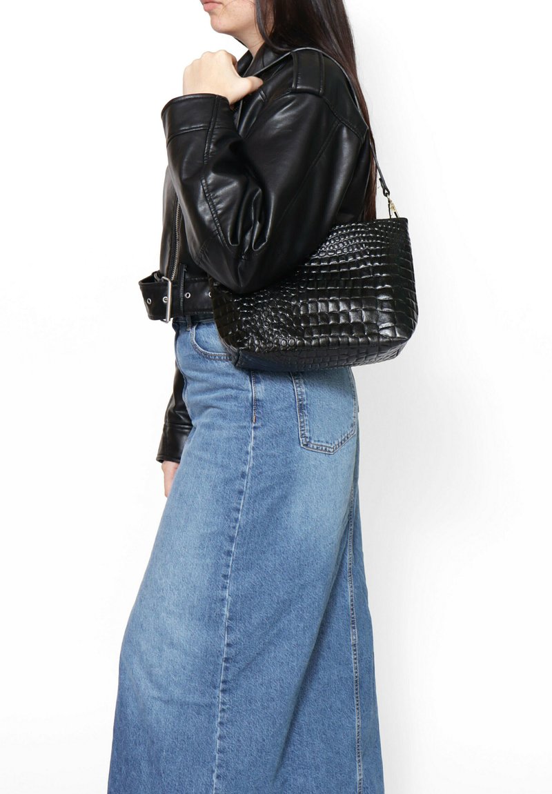 Borsa nera in pelle con stampa a croco, dalla forma strutturata e con tracolla corta, abbinata a una giacca di pelle nera e una gonna di jeans.