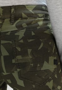 Gröna jeans med camouflagemönster, tillverkade av bomullsblandning, med en figurnära design, bakfickor och subtil detalj med svart etikett.
