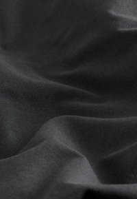 Schwarzer Stoff mit einer strukturierten, matten Oberfläche. Er zeigt sanfte Falten und Knicke, die auf ein leichtes, flexibles Material hinweisen.