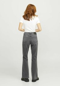 Jeans grigi con forma svasata, dotati di tasche posteriori e di un'etichetta nera sulla cintura, abbinati a una t-shirt bianca aderente.