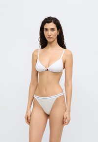 Λευκό σουτιέν με τριγωνικό σχήμα και λεπτές τιράντες, με μικρό λογότυπο στο κέντρο. Γκρι σλιπ τύπου tanga με κορδέλα μέσης με σήμα, λιτός σχεδιασμός και απαλή υφή.