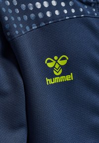 Tessuto atletico blu navy con superficie testurizzata, caratterizzato da un logo "hummel" verde e una sezione decorata con punti blu e argento.