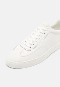 Witte leren sneaker met een getextureerde tong, ronde neus en platte veters. Heeft een eenvoudig, glad ontwerp en een contrasterende stikseldetails.