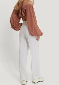 Bluzka z odkrytymi ramionami i bufkami w kolorze rdzy, zestawiona z lekkimi białymi lnianymi spodniami. Sportowe buty dopełniają stylizację.