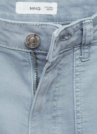 Svetlo modré denimy džínsy s kovovým strieborným zapínaním na gombík a zipsom, s jemne štruktúrovaným povrchom. Na vnútornej strane pásu je viditeľná nálepka.