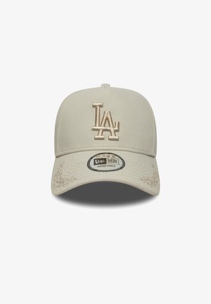 Beige cap with a structured design, featuring a raised beige "LA" logo, textured fabric, and a curved visor. Adjustable strap visible.