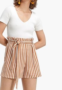 Top blanco de manga corta con textura acanalada combinado con pantalones cortos de talle alto a rayas marrones y blancas, con lazada frontal y bolsillos.