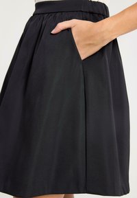 Gonna nera con vita arricciata e tasca laterale, realizzata in un tessuto liscio e testurizzato, con un taglio che arriva al ginocchio.