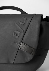 Borsa a messenger nera con una finitura testurizzata, dotata di chiusura con patta, marchio in rilievo e tracolla in pelle con cuciture precise.