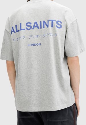 Person trägt ein graues T-Shirt mit blauem Text "ALLSAINTS" und "LONDON" sowie japanischen Zeichen auf dem Rücken.