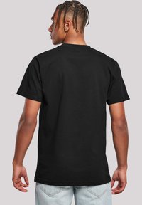 Black cotton t-shirt with a classic crew neck, short sleeves, and a straight hem, worn with light blue denim jeans. Rear view shown.