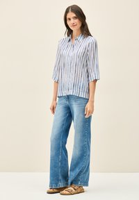 Camicia button-up con righe blu e bianche, maniche a tre quarti. Abbinata a jeans a gamba larga azzurri e sandali marroni.