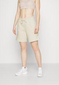 Pantalones cortos deportivos de color beige claro con cintura elástica y cordón. Combinados con un sujetador deportivo a juego y zapatillas blancas.