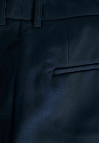 Marinblått tyg med en slät textur, som har en platt framsida, synliga sömmar och en detalj med en enda sidoficka.